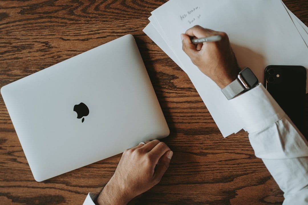 Professional person working on resume at laptop with papers spread on desk
